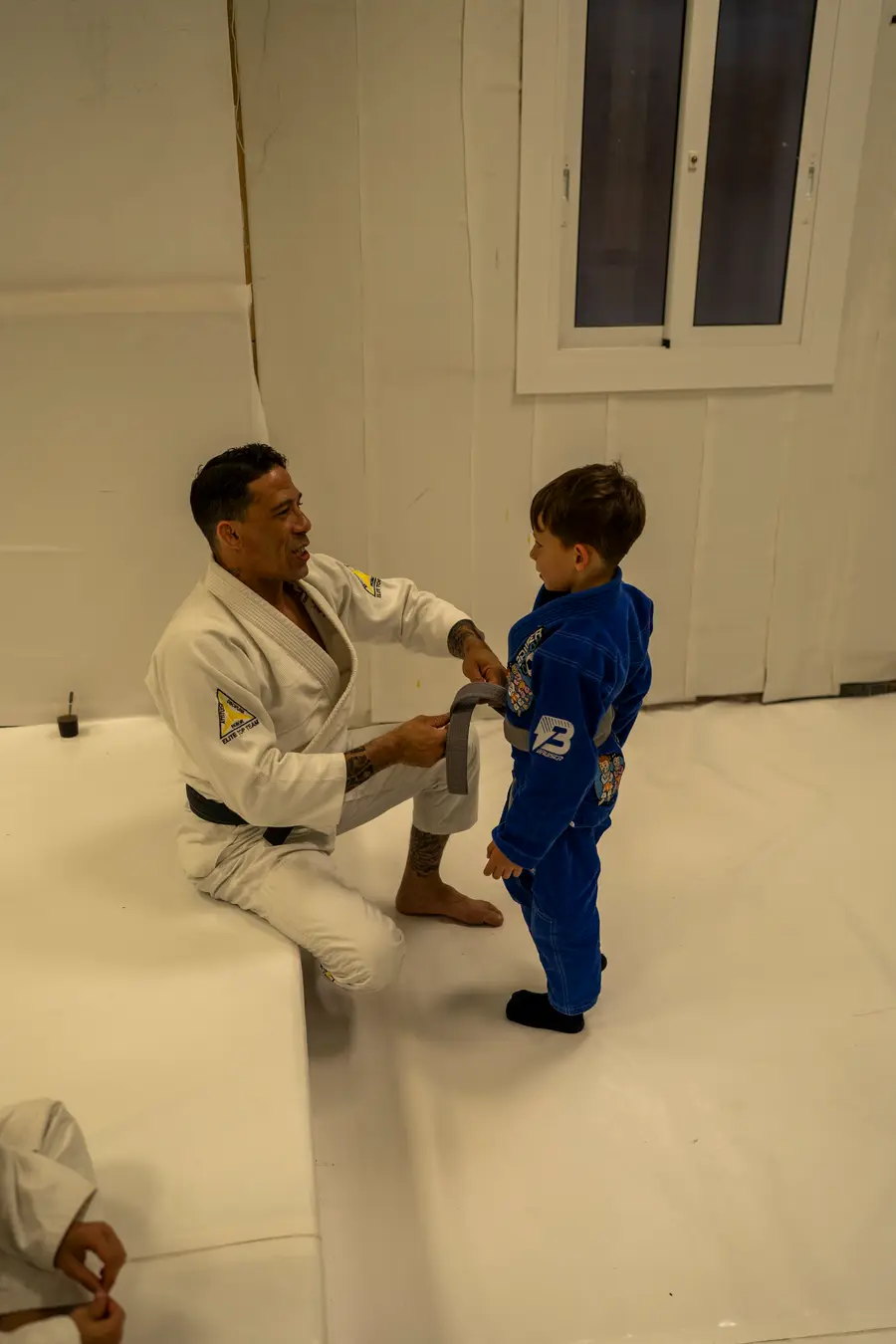 Instructor anudando el cinturón a un alumno infantil, de espaldas